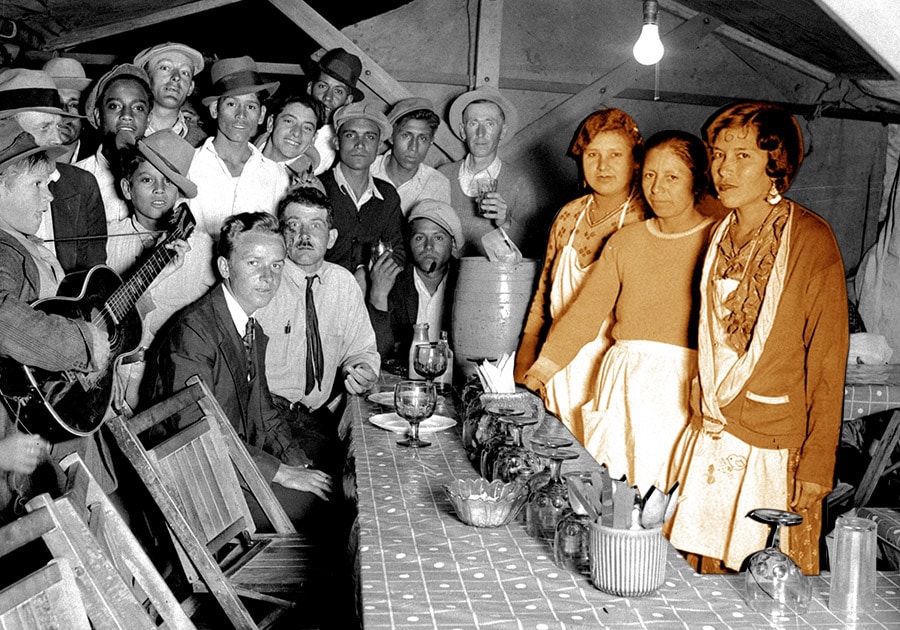 old photo of three chili queens and a group of men inside a tent, eating, drinking and smoking.